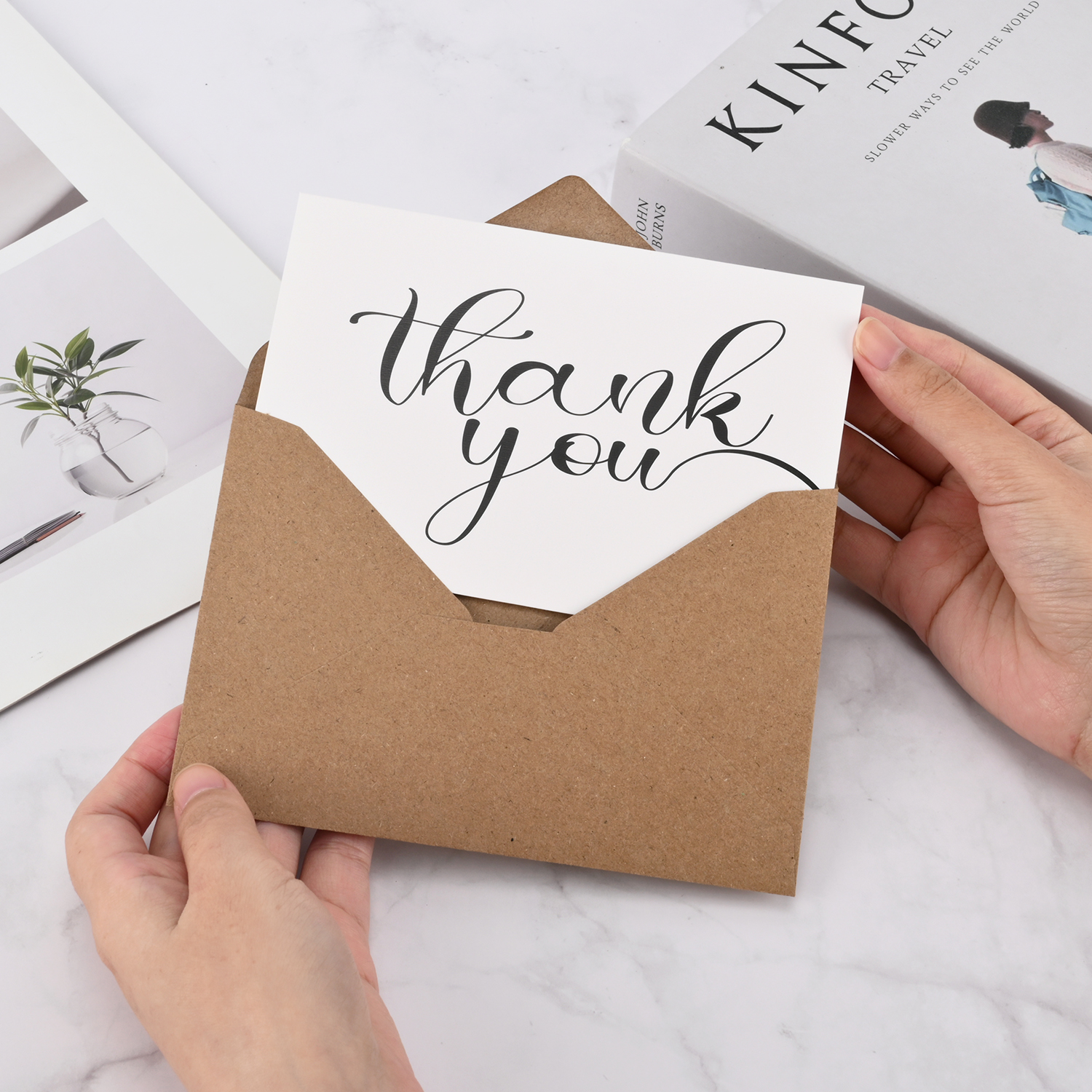 Printed thank-you card being placed inside a kraft paper envelope